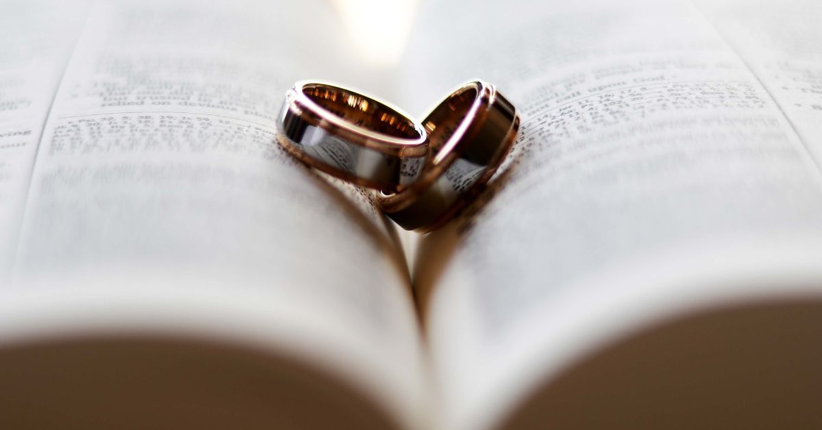 Anillos de boda de oro entrelazados sobre un libro abierto que forma un corazón en sus páginas, simbolizando el amor y el compromiso durante un permiso retribuido.